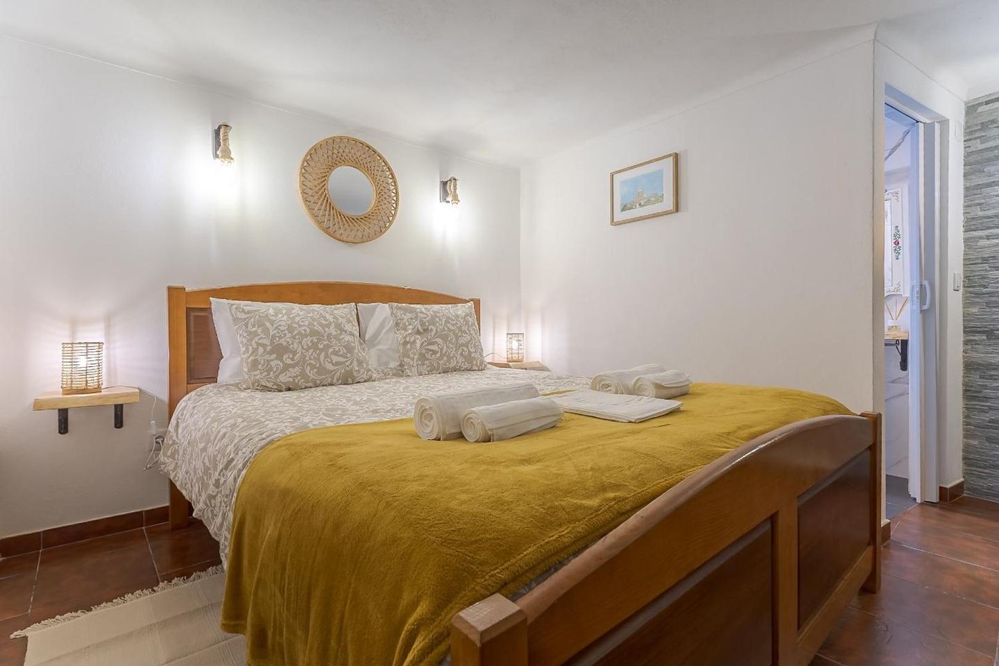 Suite com cama king size, colcha cor de mostarda e candeeiros de parede