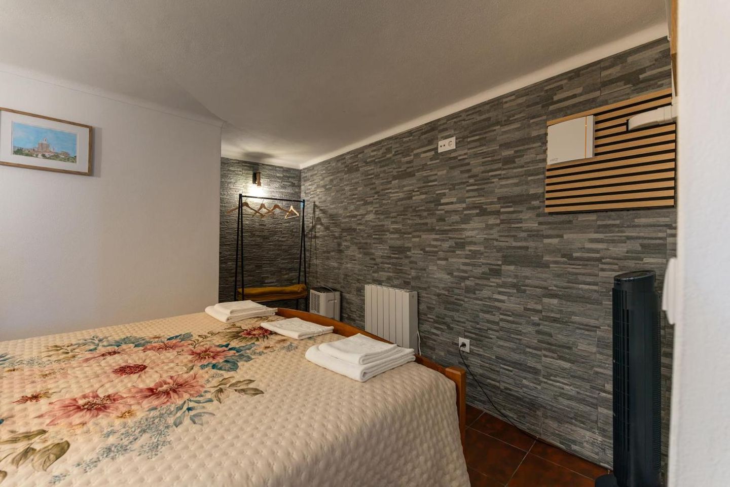 Quarto de casal com parede revestida a pedra e colcha de flores